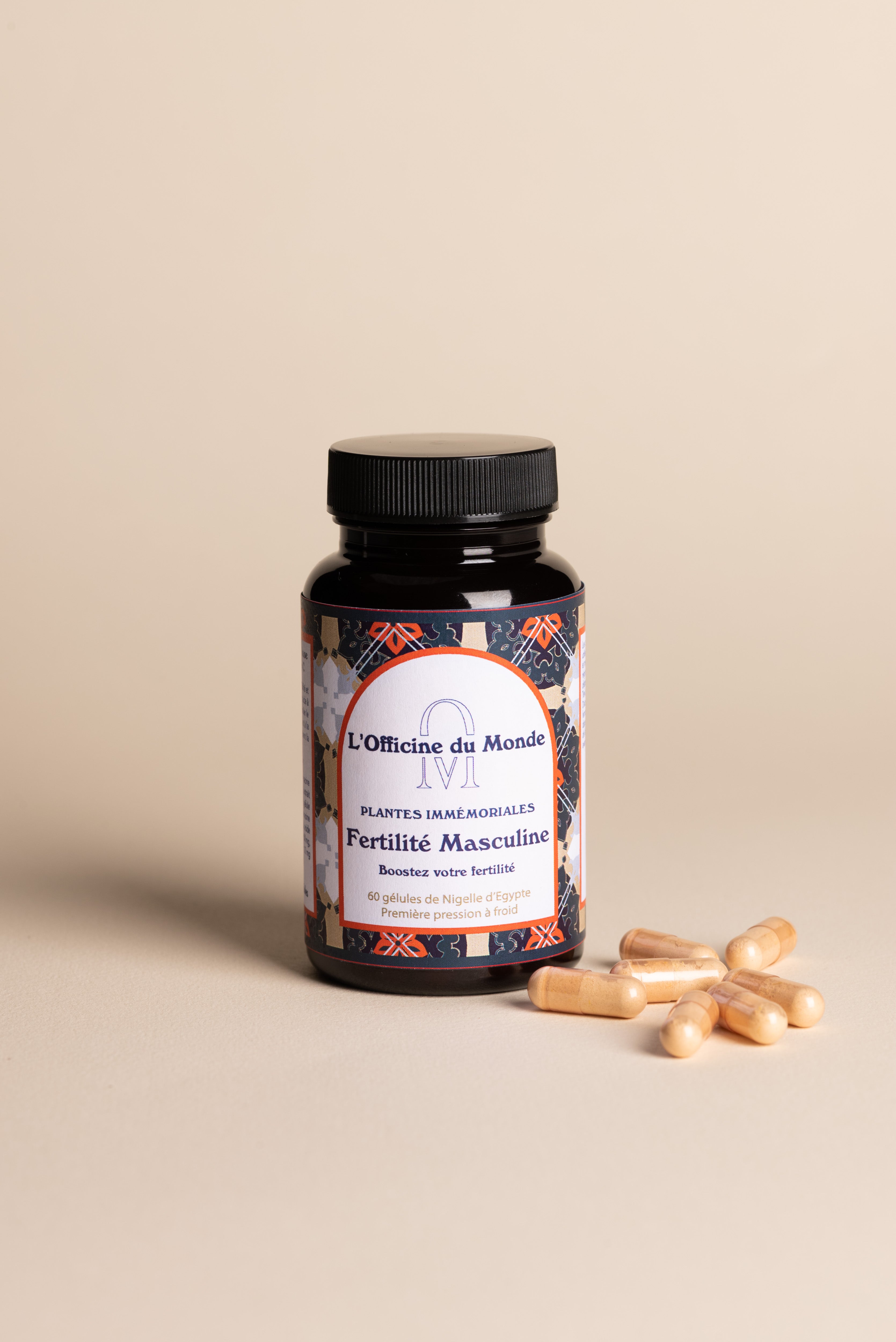 Flacon en verre brun du complément alimentaire « Fertilité Masculine » de L’Officine du Monde, avec bouchon noir et étiquette aux motifs orientaux foncés, posé sur une surface beige, accompagné de plusieurs gélules végétales disposées à côté.